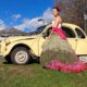 Photo de Mélodine portant la robe florale dans un champ, à côté d'une voiture vintage