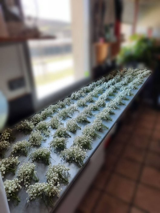 Table avec des dizaines de mini bouquets en préparation pour la création d'une robe florale