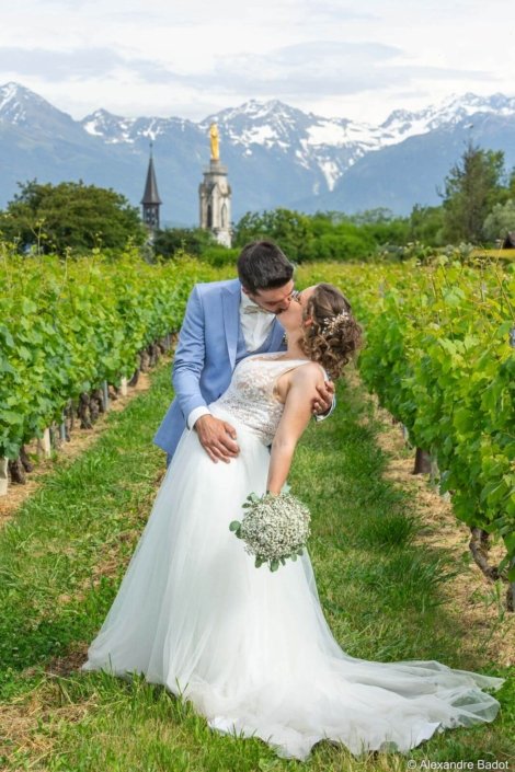 Photo de Chloé et Paul dans un champ, avec en arrière plan l'église et des montagnes enneigées
