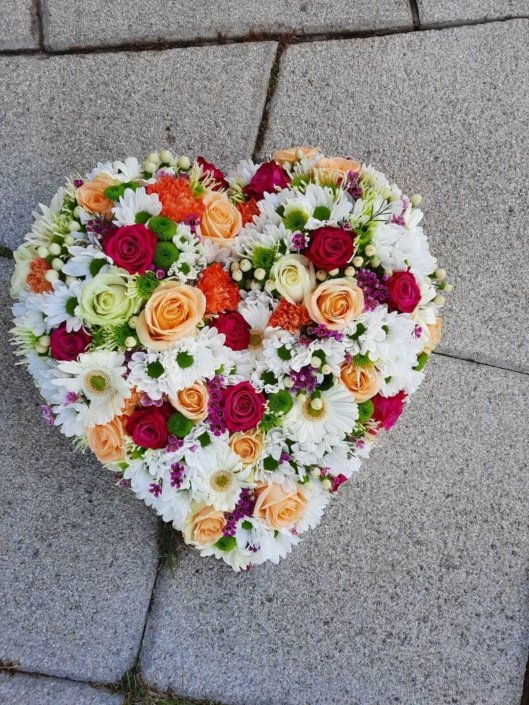 Composition florale blanche avec des rose colorées en forme de cœur, pour le deuil