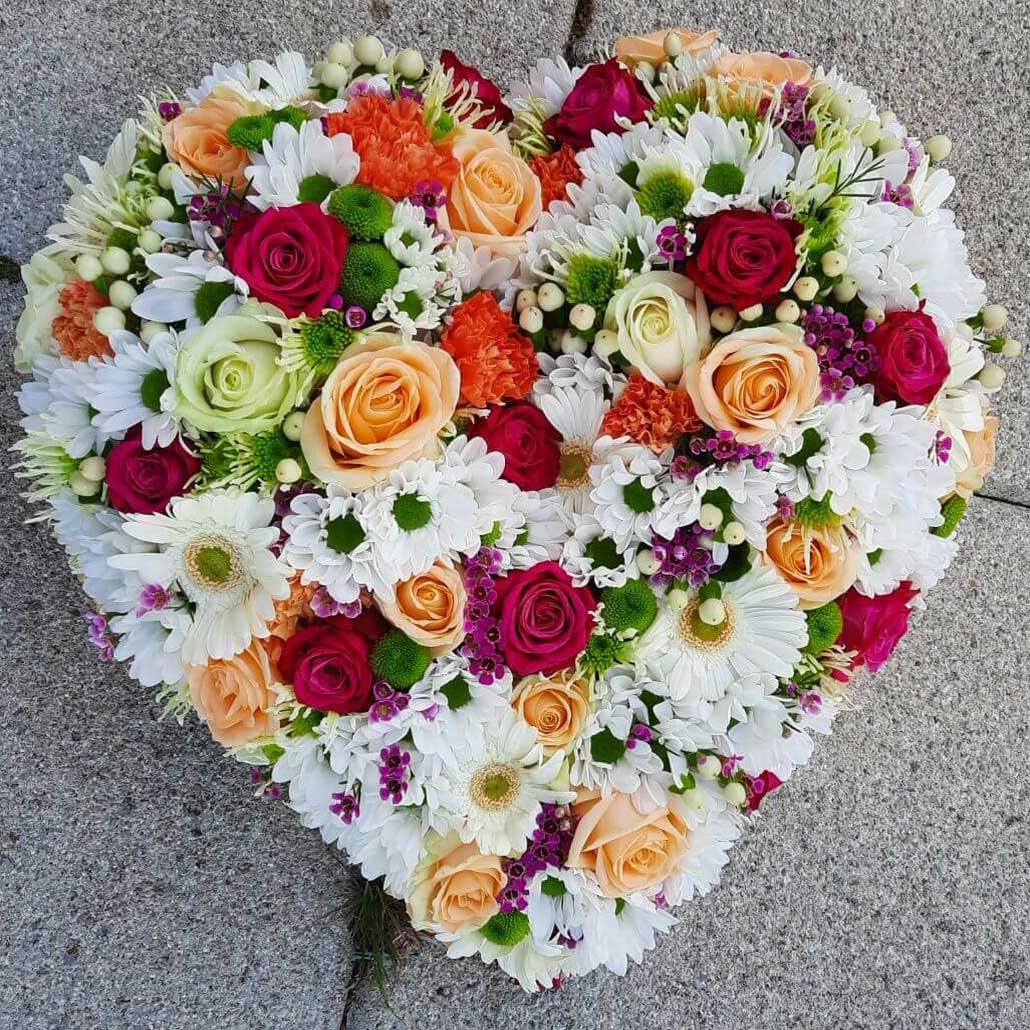 Composition florale blanche avec des rose colorées en forme de cœur, pour le deuil